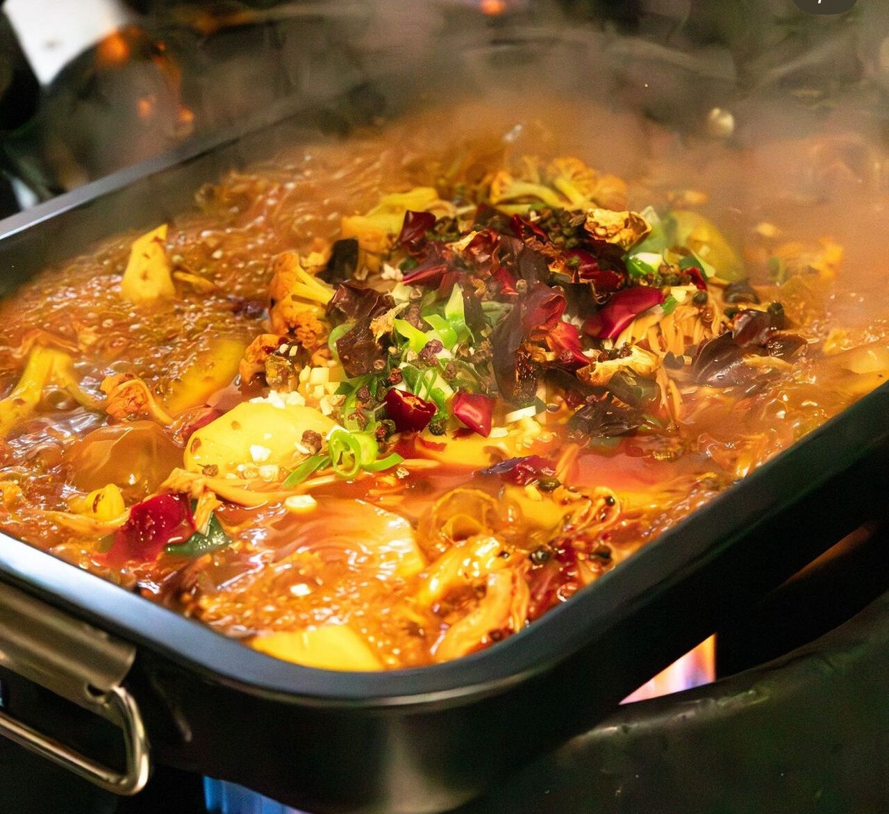 Scodella di fuoco fumante sul fornello, brodo rosso con peperoncini secchi.